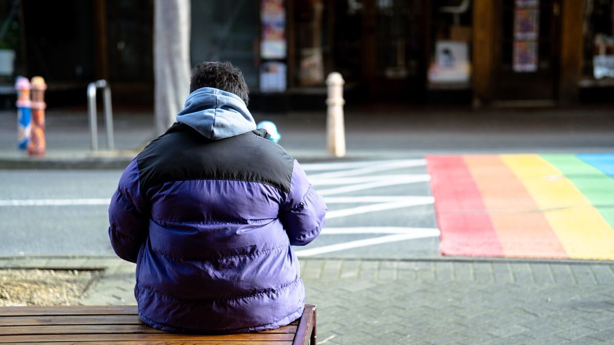 Person sitting near rainbow crosswalk
