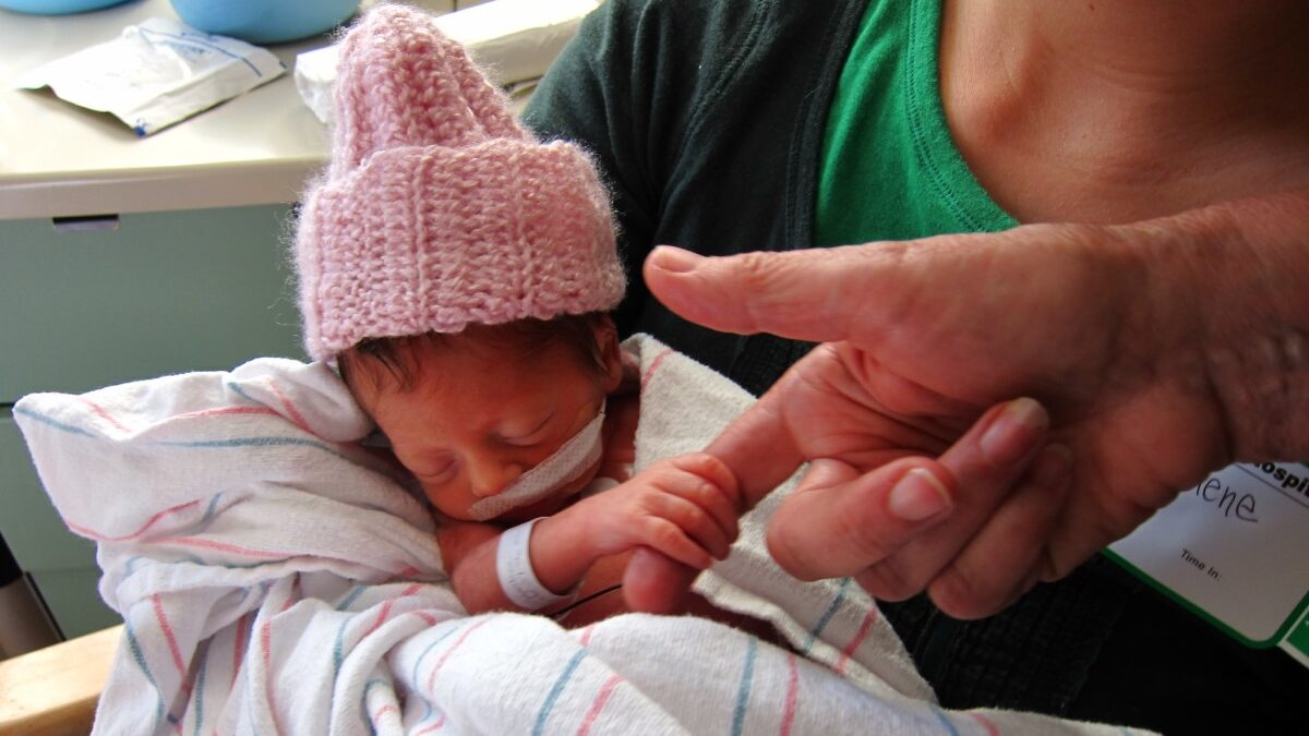 Preemie infant holds a grownup's finger tight