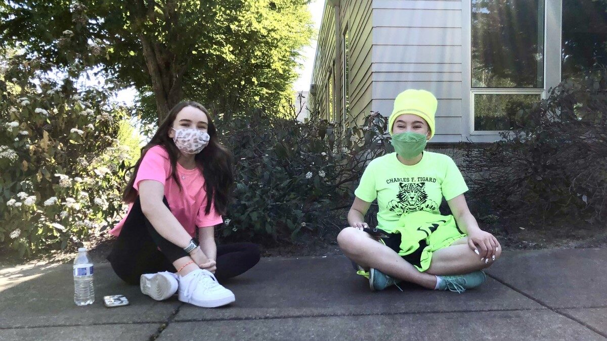 Two middle schoolers sit outside with masks on