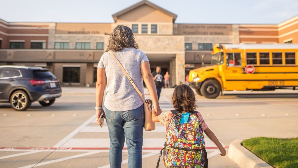 mom holding kid's hand walking into school