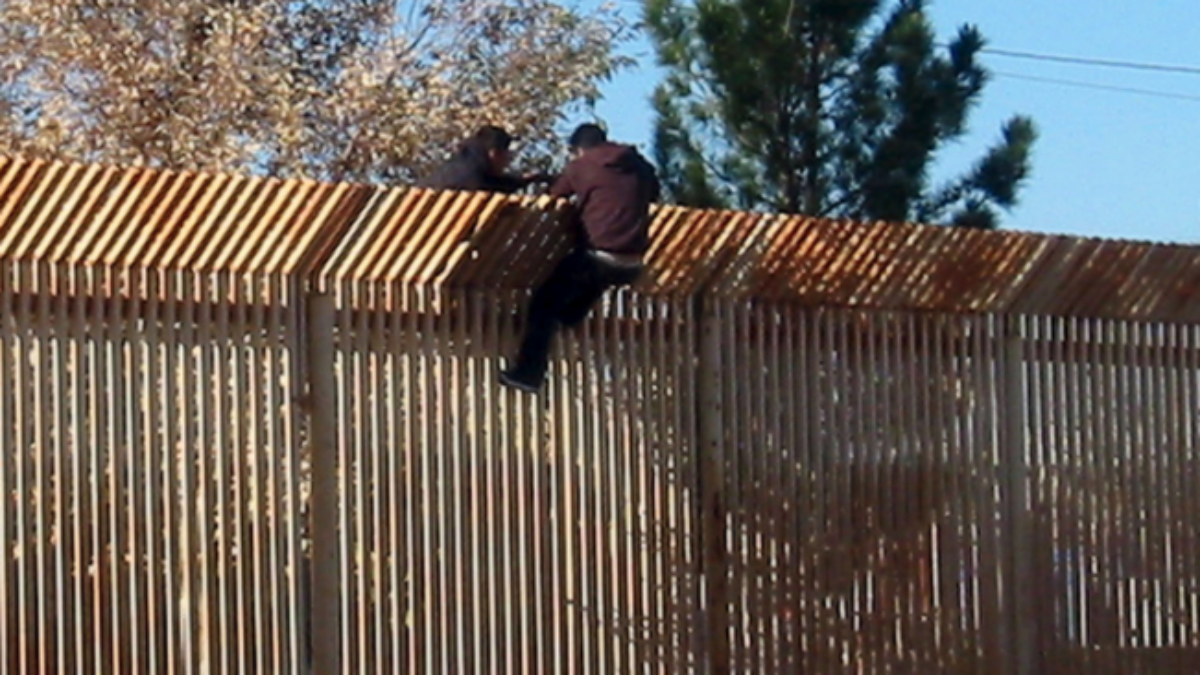 migrants scaling border wall
