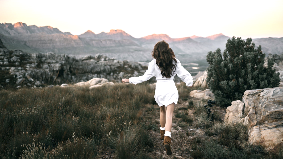 Girl in white dress running through nature landscape