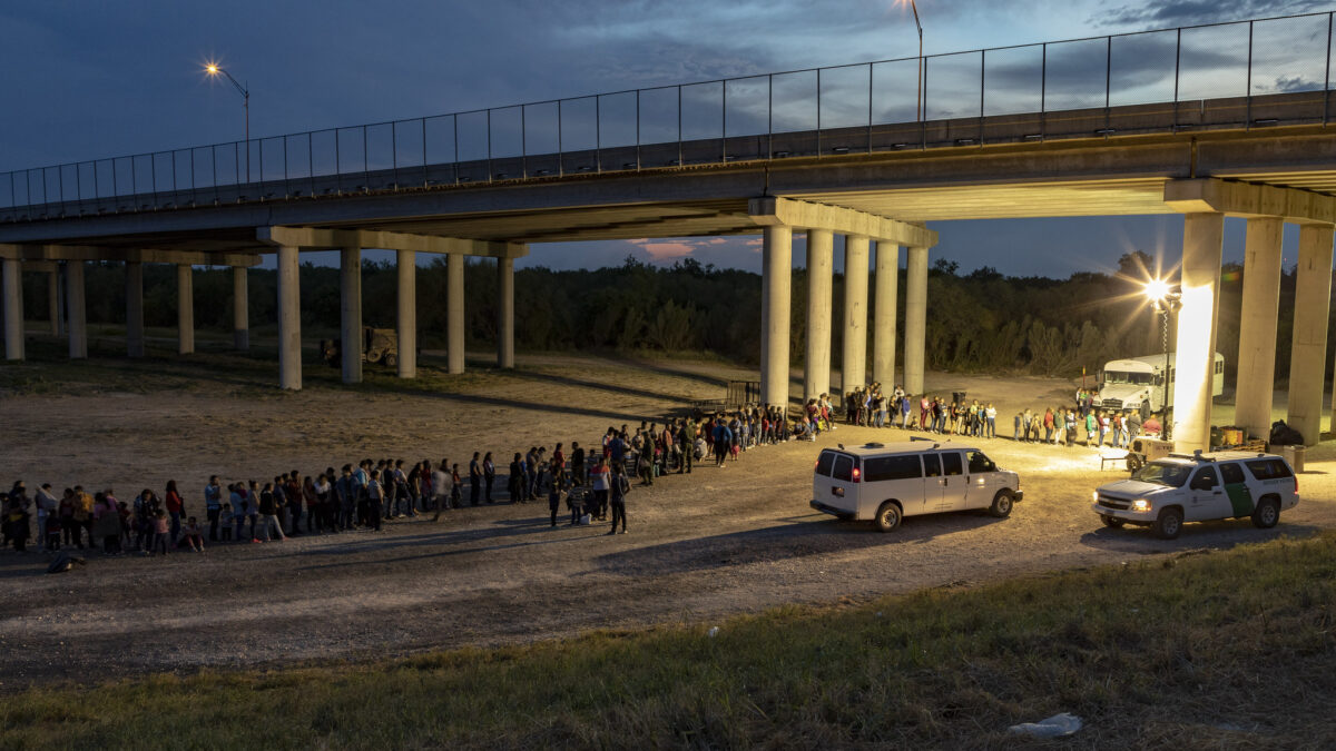 migrants in line under a bridge