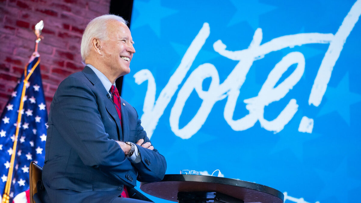 Biden sitting on chair in front of sign that says vote