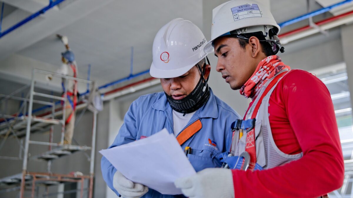 Two construction workers look over paperwork at a construction site.