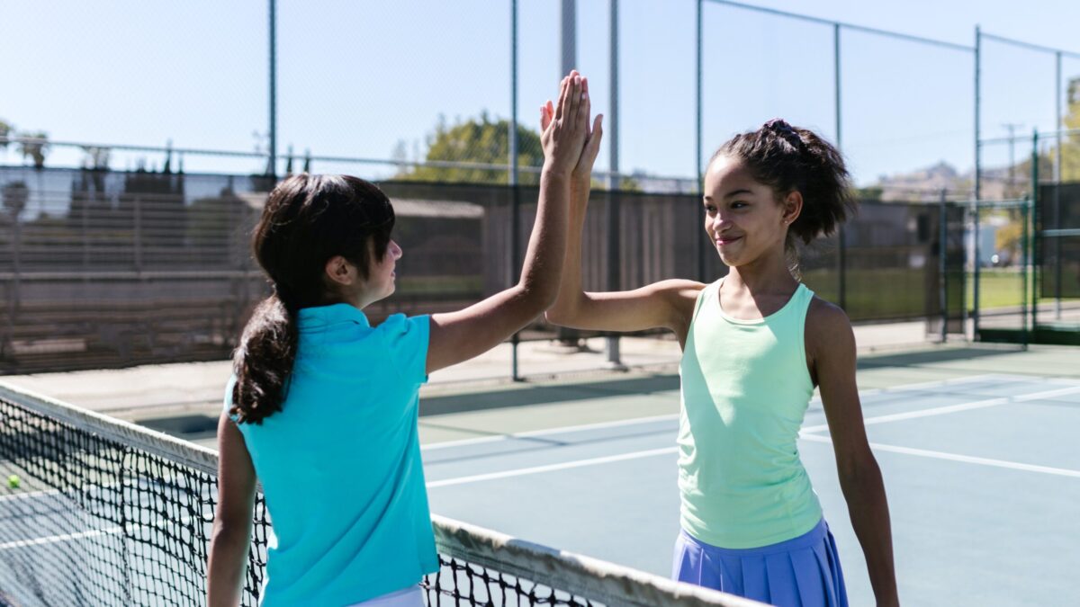 Two girls high-five each other while playing tennis.