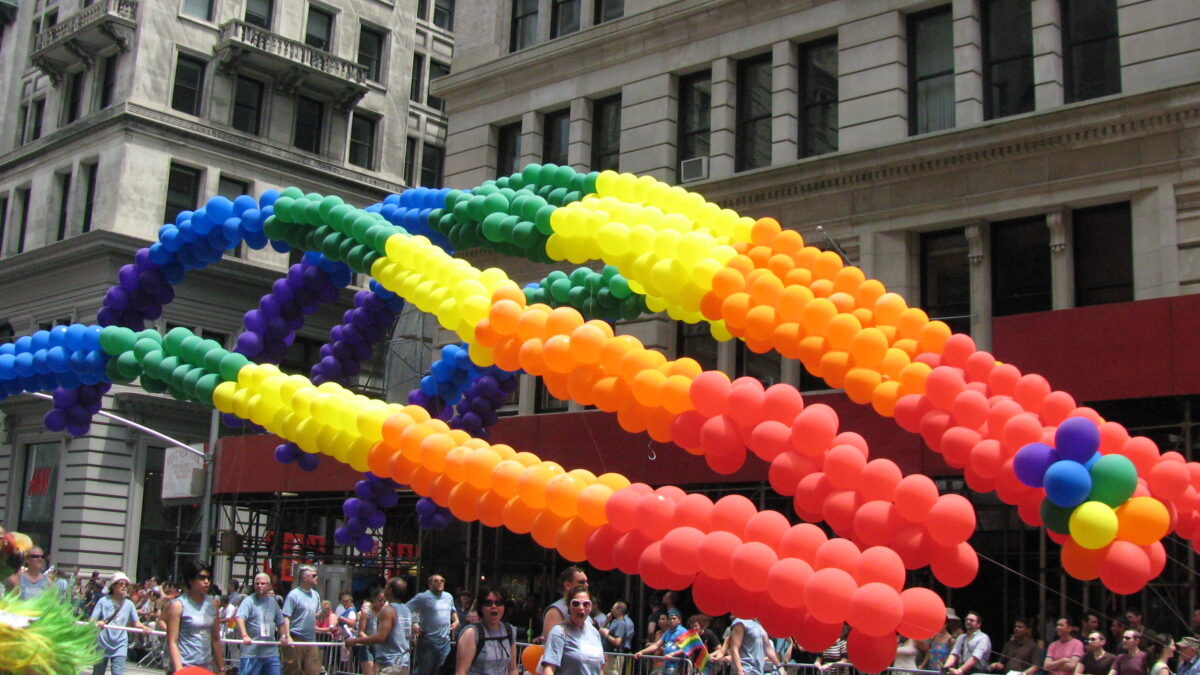 Rainbow balloon arches fly above people marching in a gay pride parade