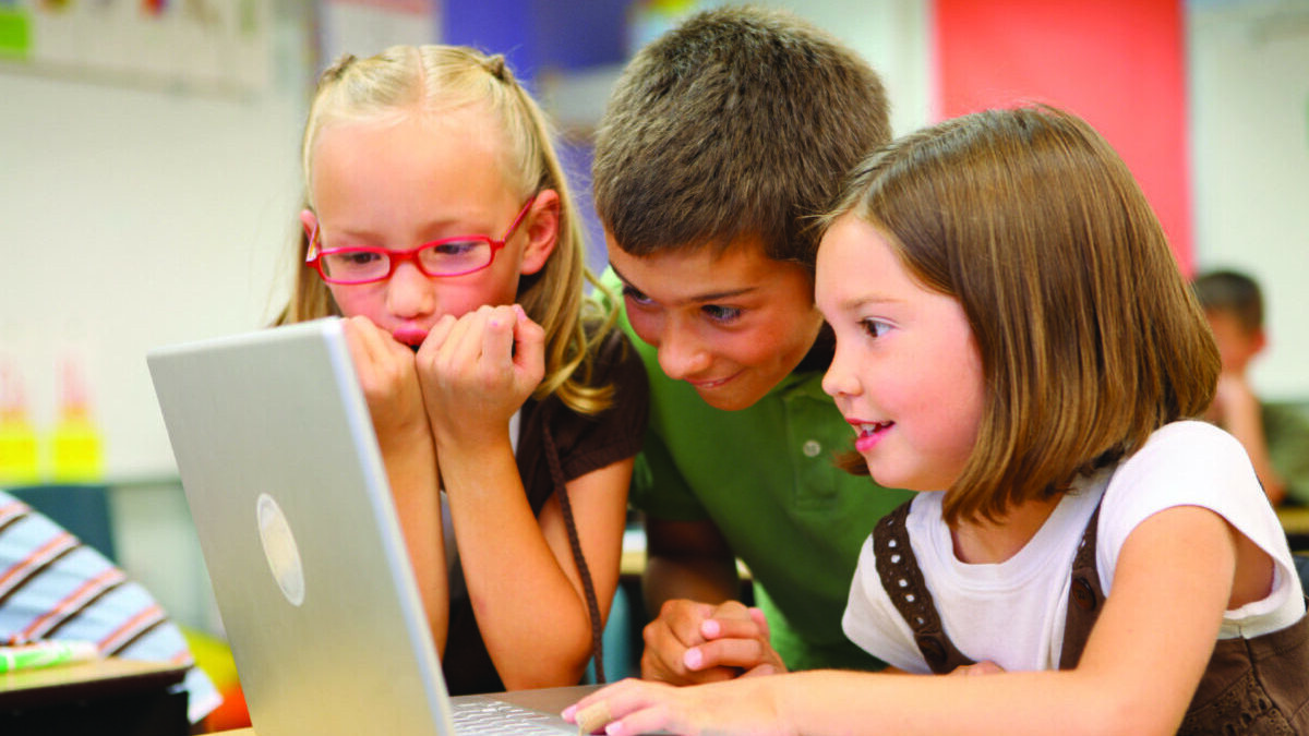 three children looking at a laptop at school