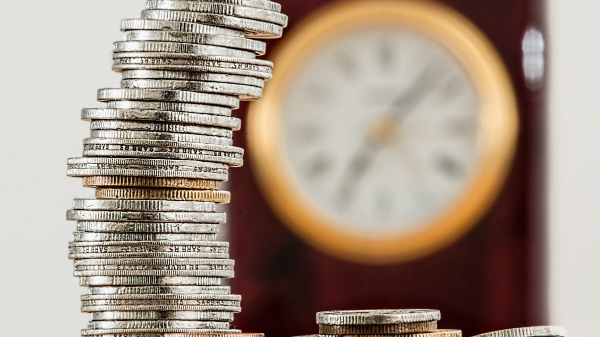A stack of coins with a clock in the background.