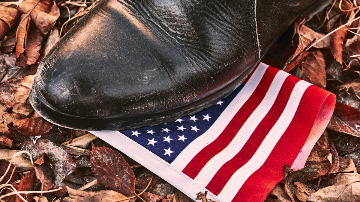 person in a boot stepping on the American flag