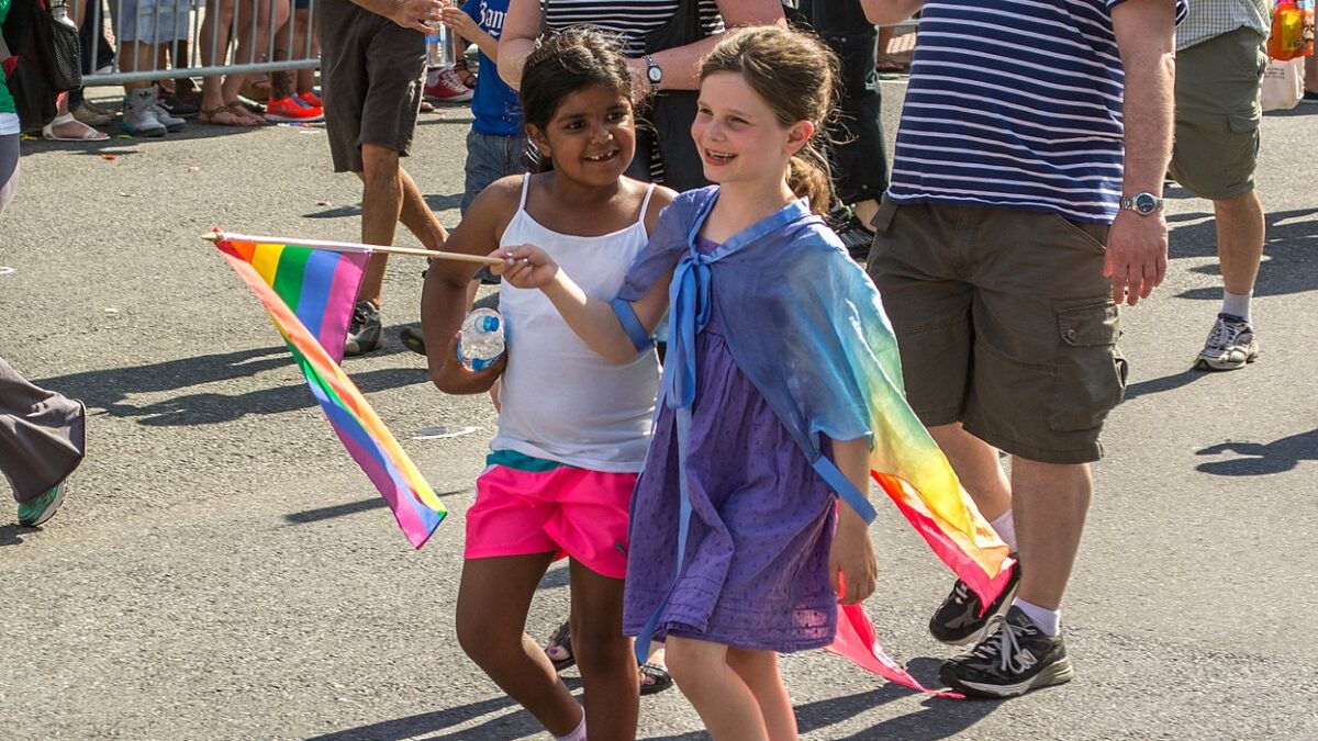 two young girls wearing rainbow colors carry pride flag in pride parade
