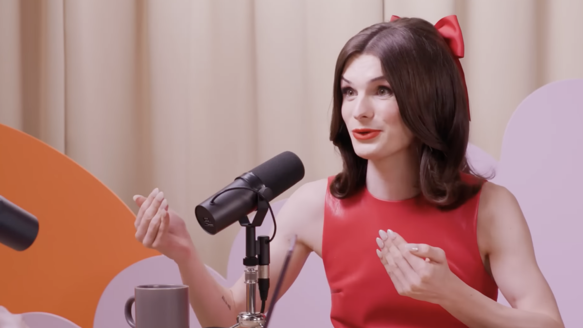 Man wearing red dress talking into mic on podcast set