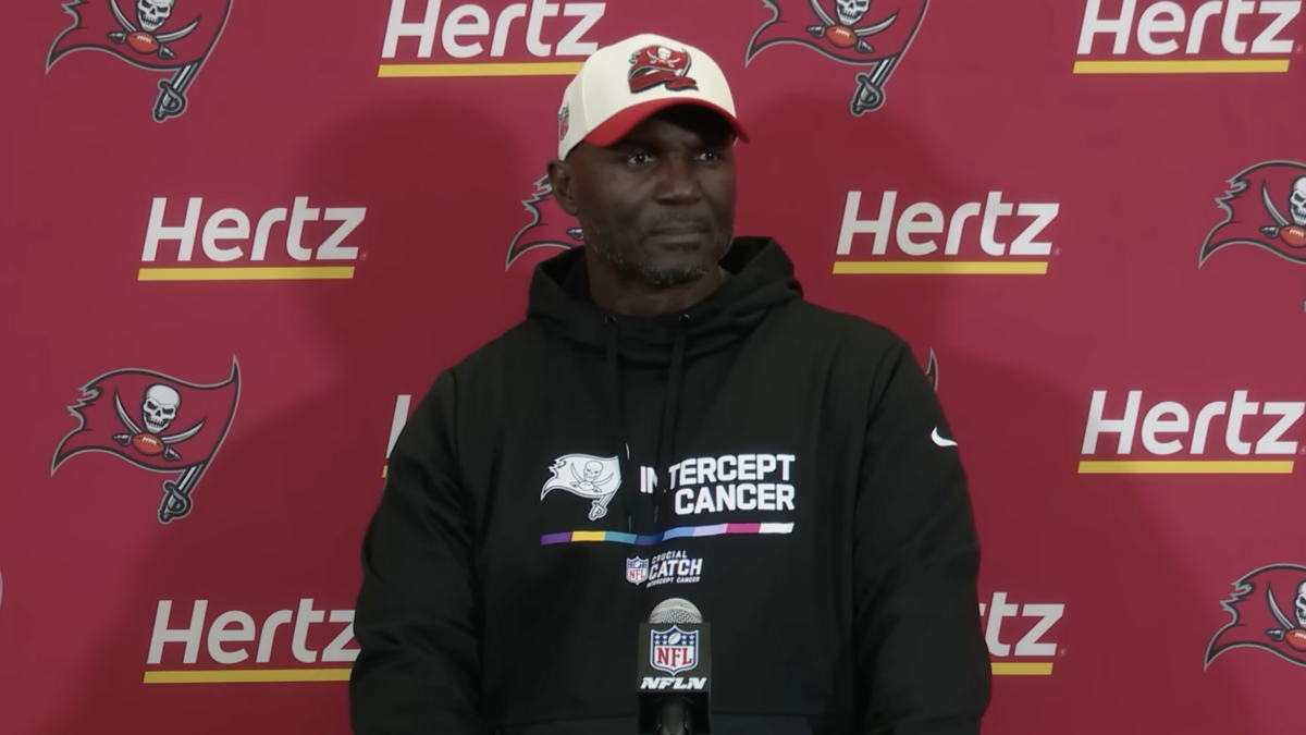black football coach Todd Bowles stands at post-game press conference in hoodie and baseball cap