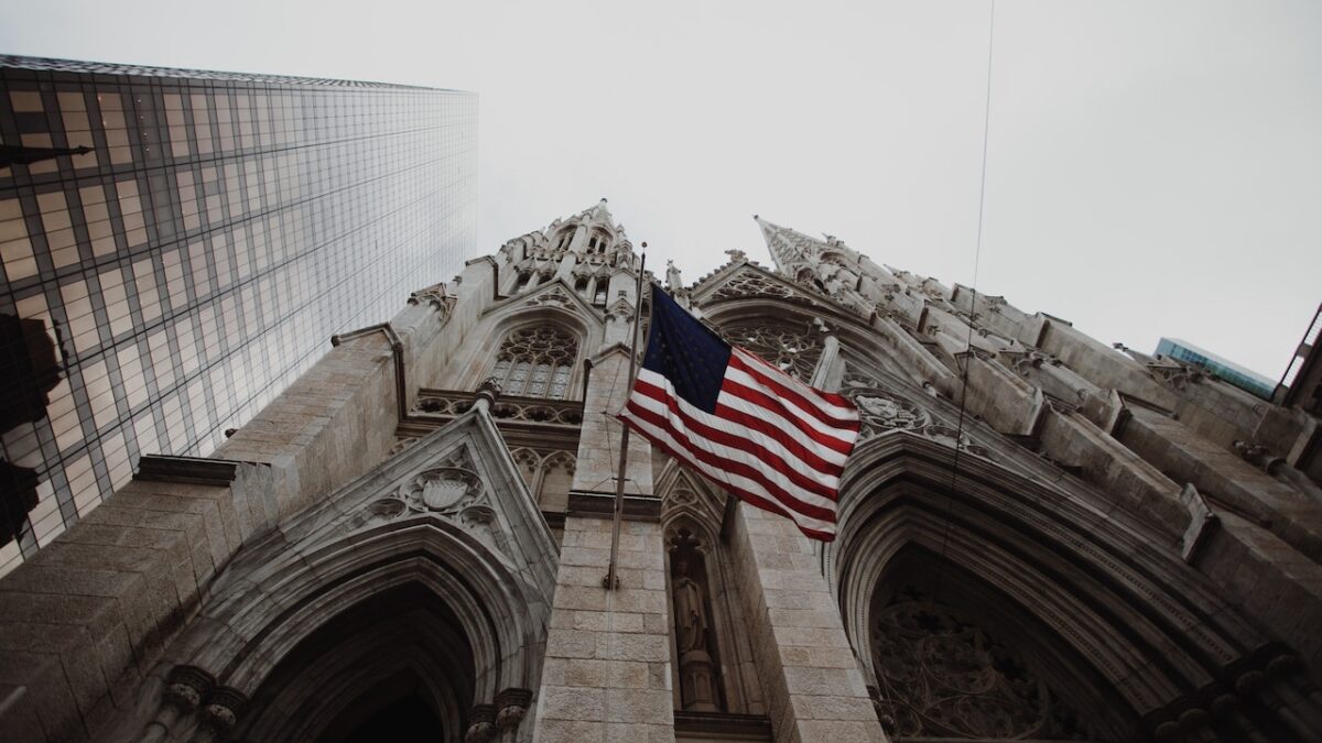 low angle photo of American flag handing from concrete cathedral