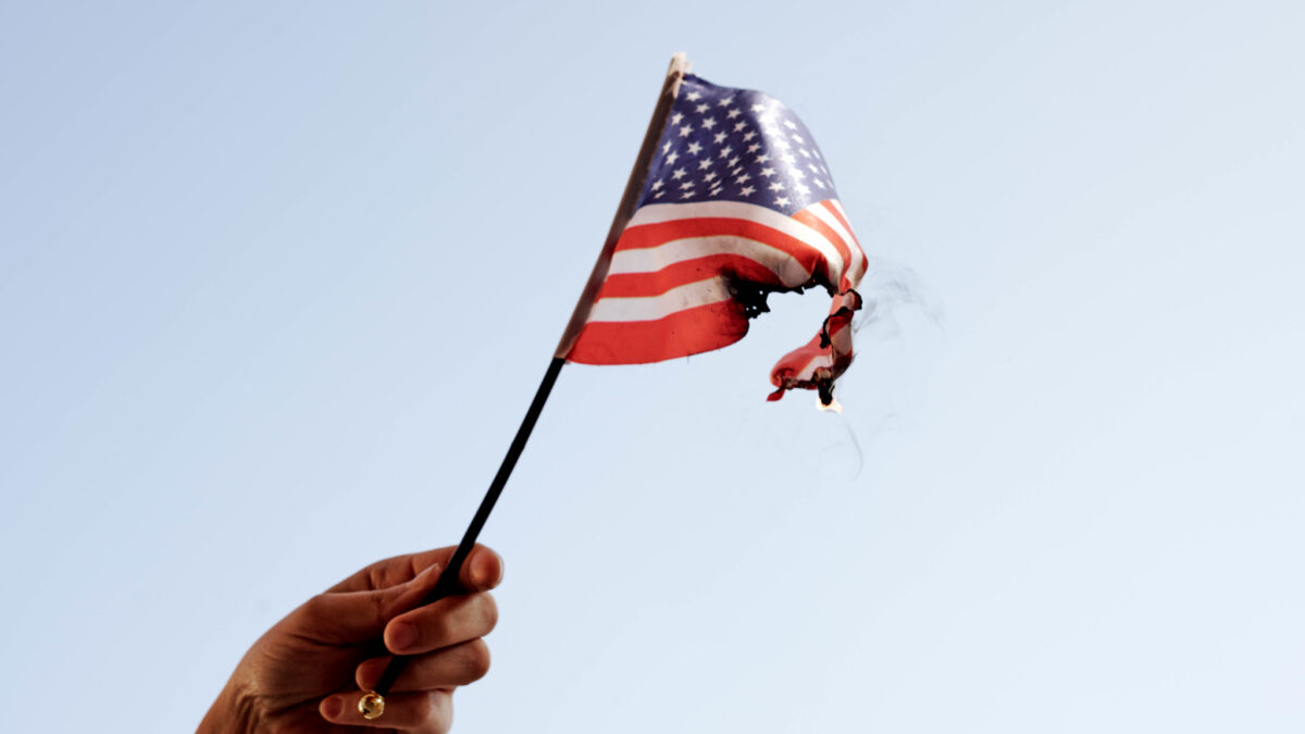 hand holding a burning American flag against the sky