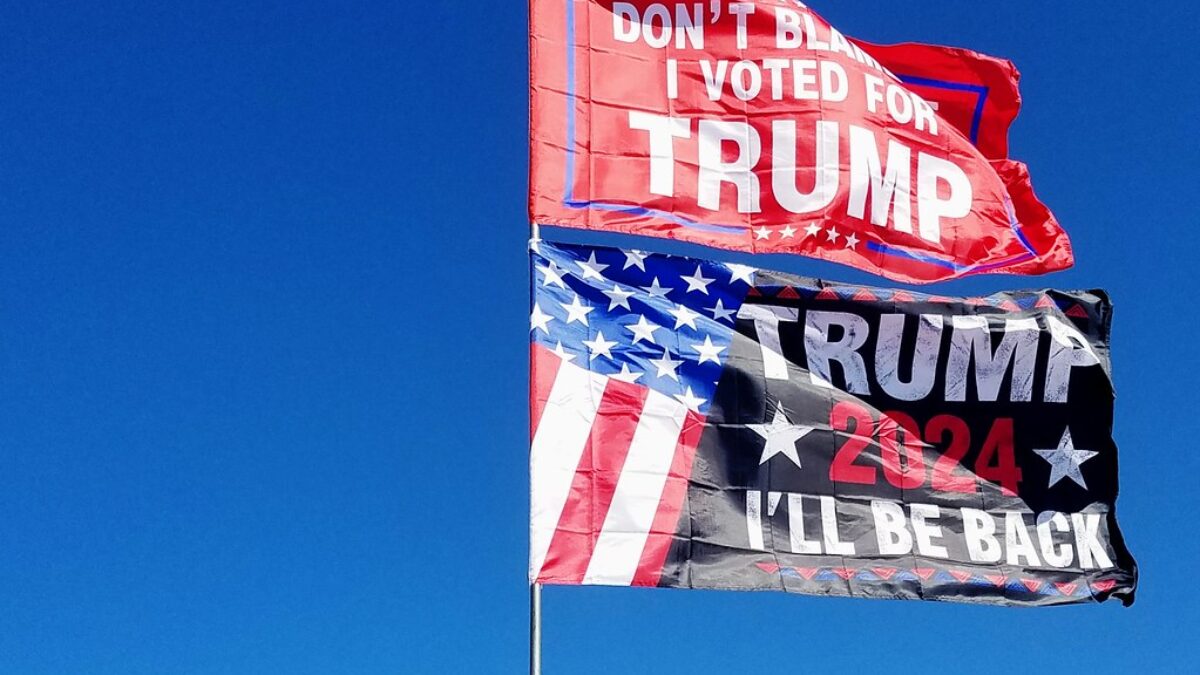 two pro-Trump flags waving from poll in blue sky