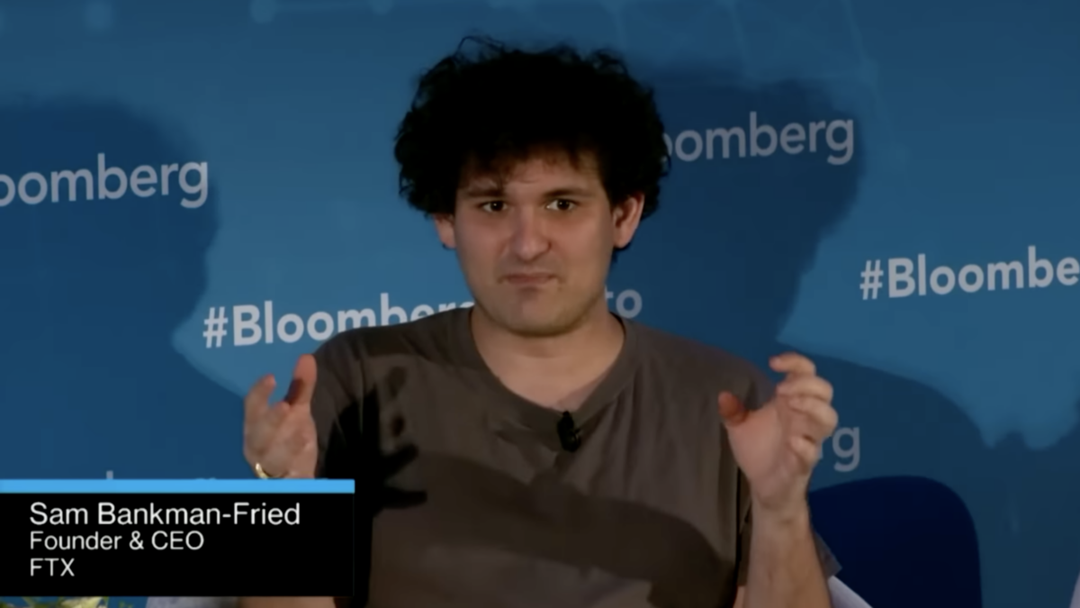 creepy crypto bro talking on stage with hands wearing brown t-shirt