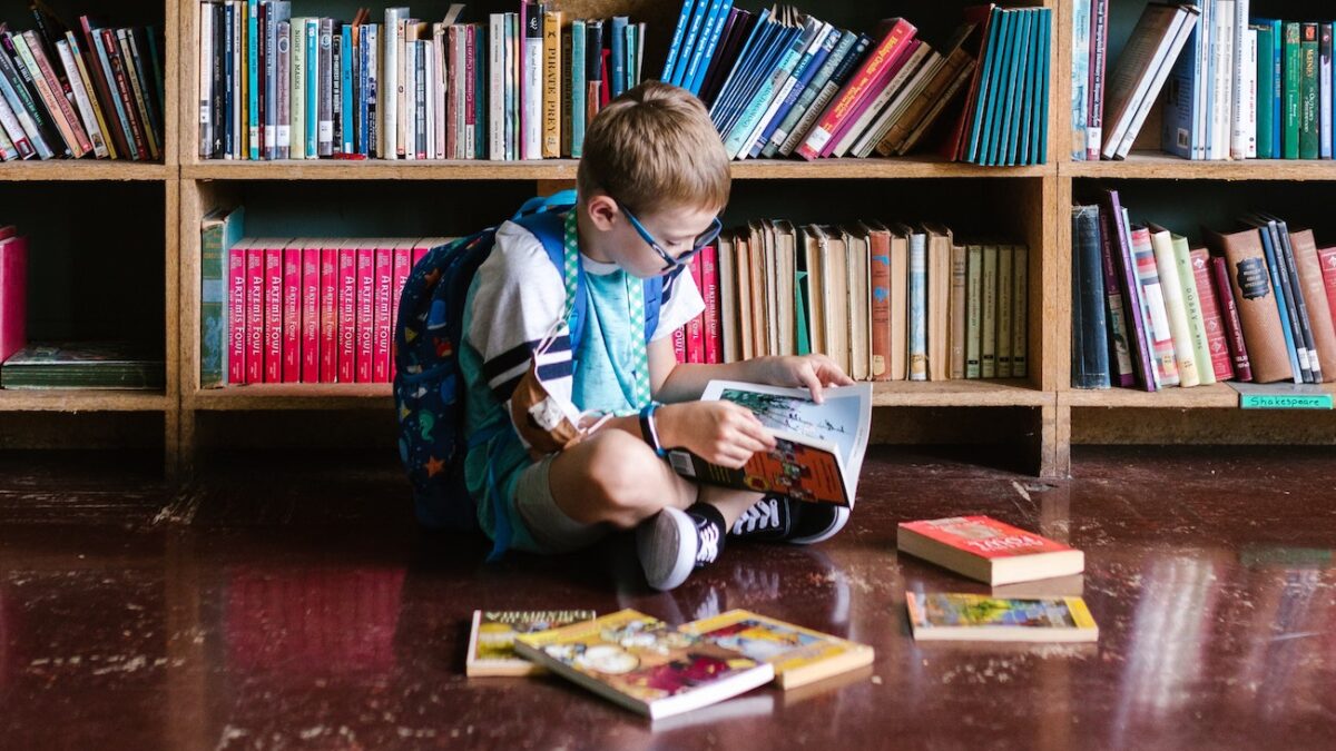 little boy reading books on floor of school library