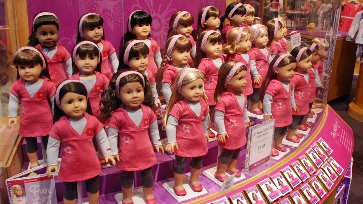 rows of American Girl dolls lined up behind glass in toy store