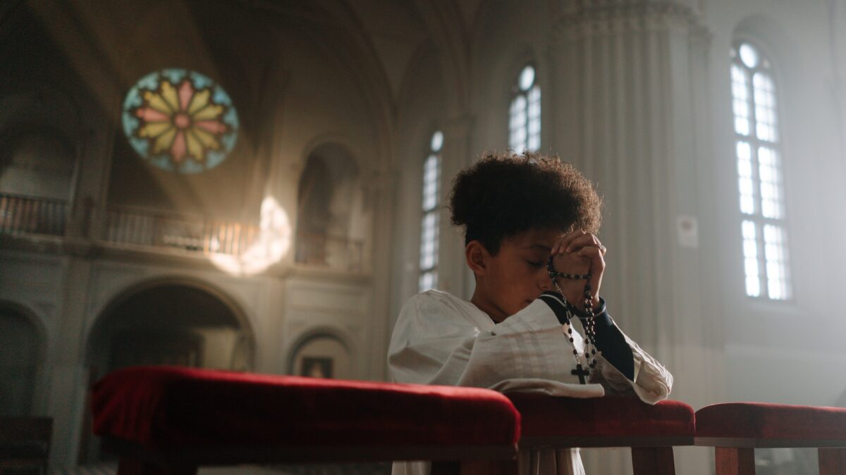Altar boy praying in church with his rosary