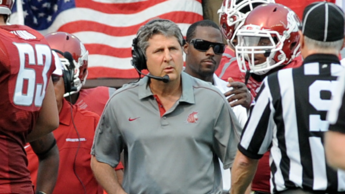 Coach Mike Leach walking on a football field surrounded by team