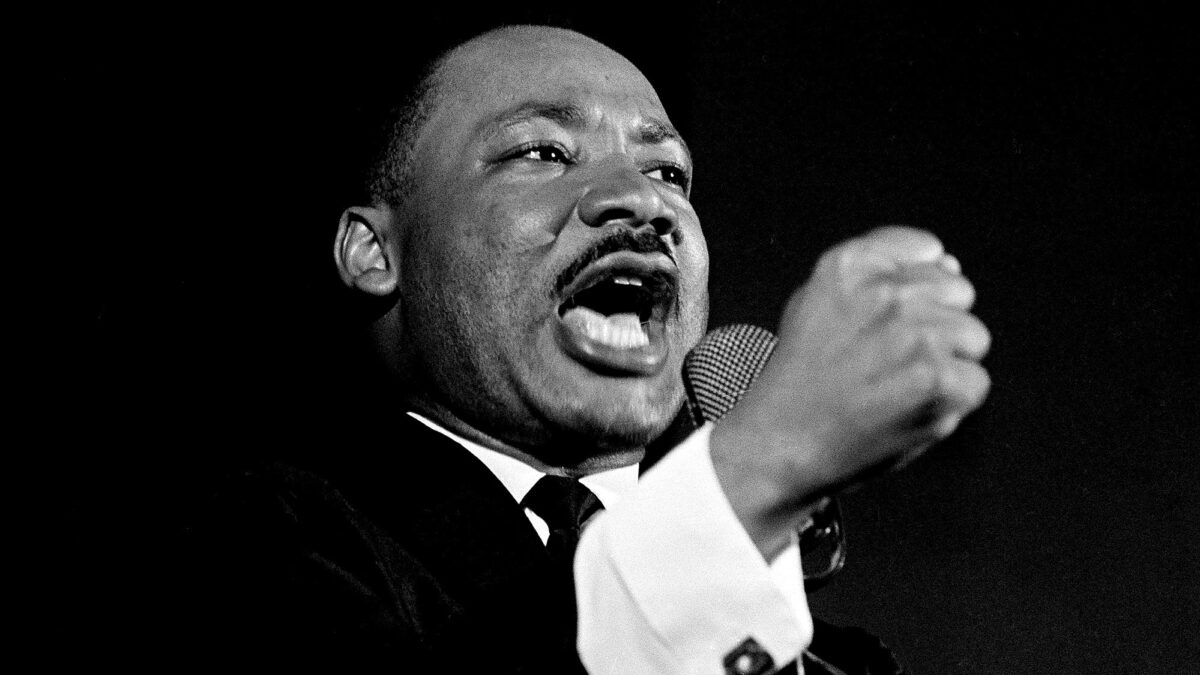 Marting Luther King Jr. holding up fist as he gives speech in front of black background