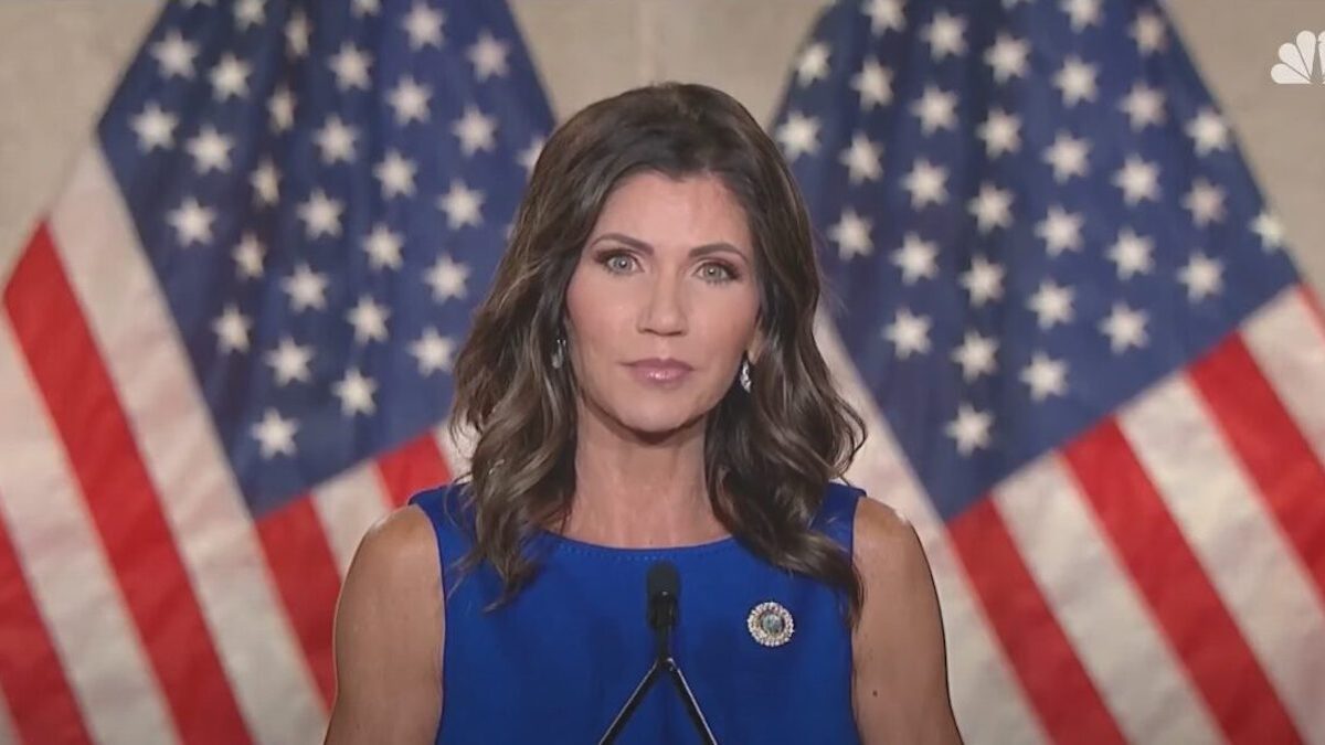 Kristi Noem in front of two American flags