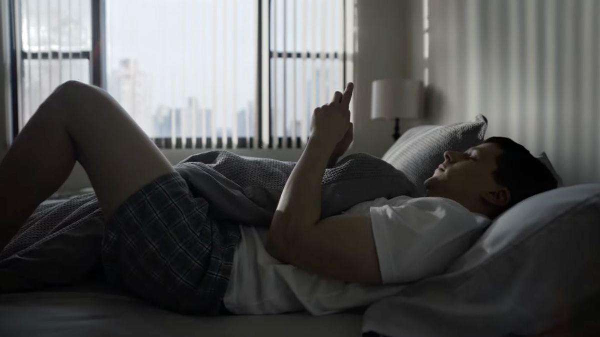 Actor in TV show laying in bed swiping on dating app on smart phone