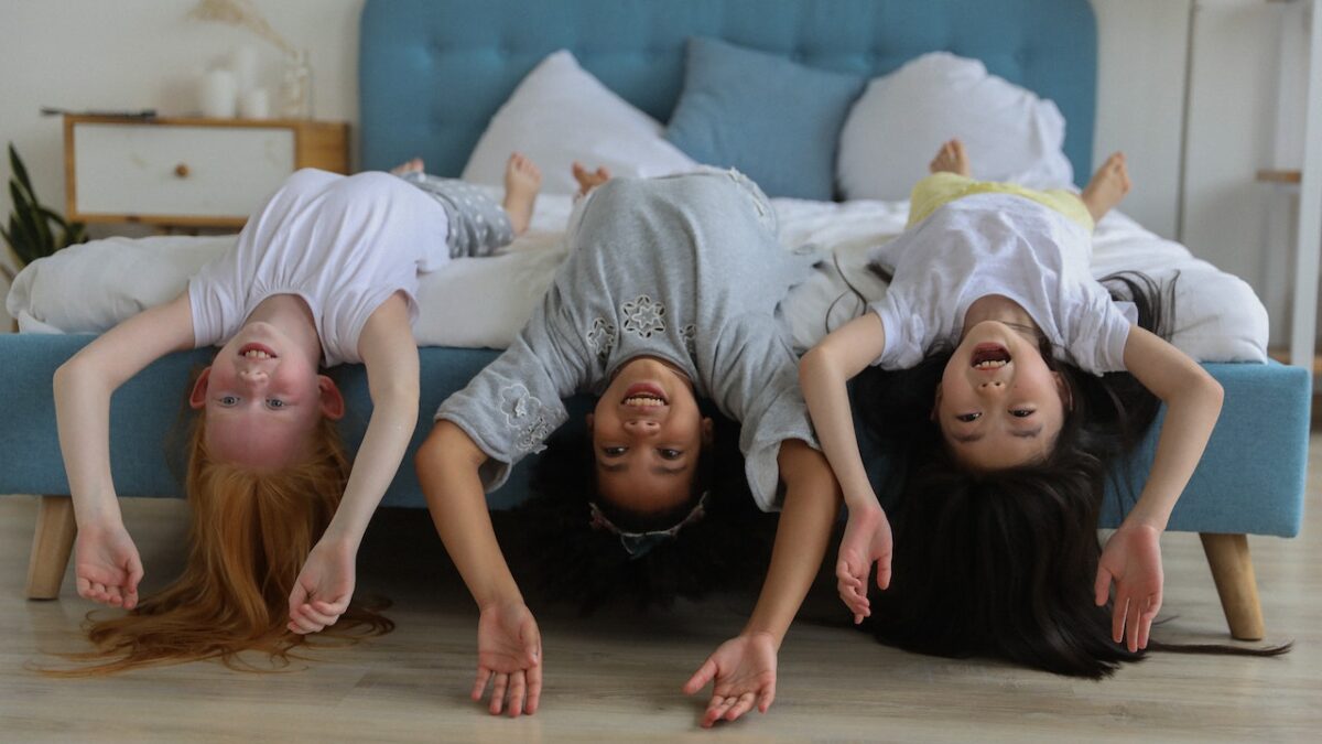 three girls laying upside down laughing on bed