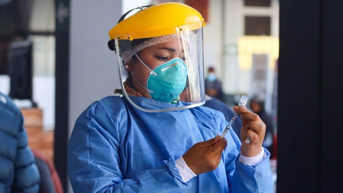 Health care worker in PPE holding a Covid-19 vaccination