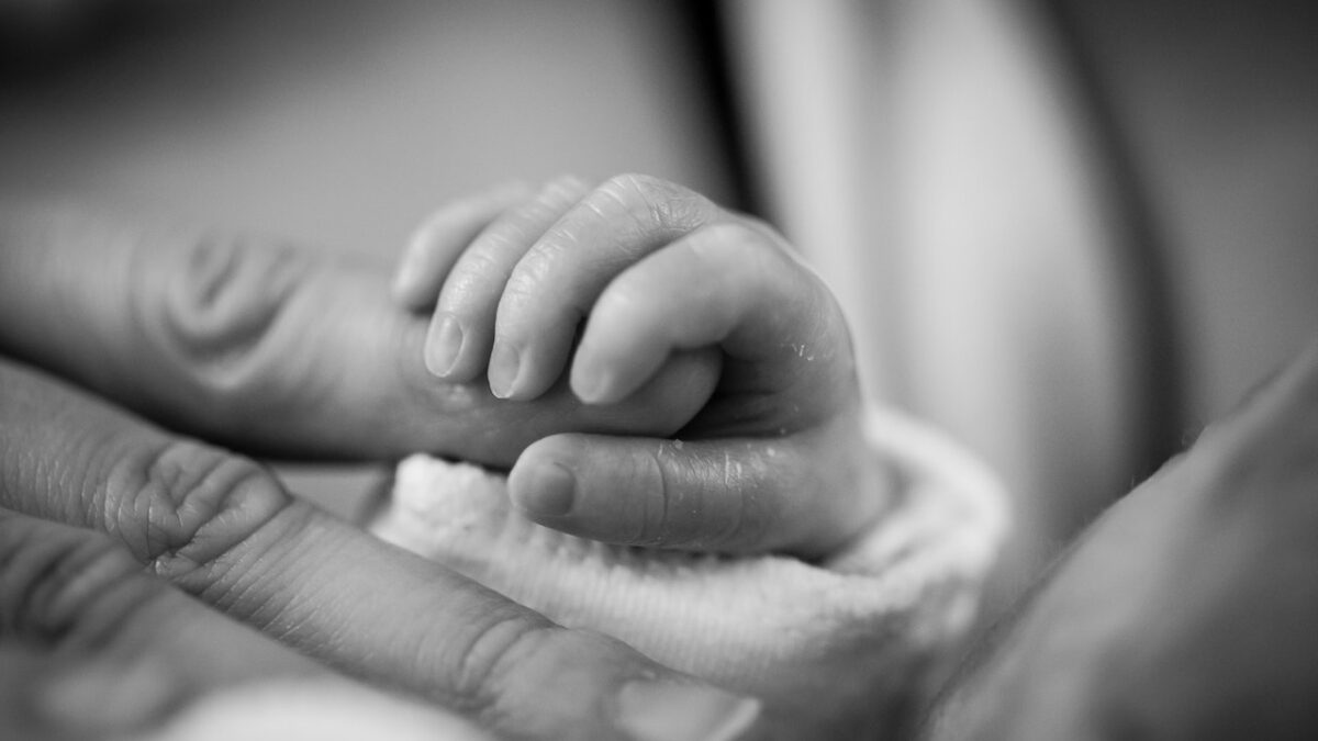 baby holding her mother's finger in black and white