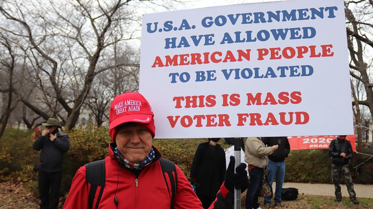 man in D.C. on Jan. 6 holding a voter fraud sign and wearing a red maga hat