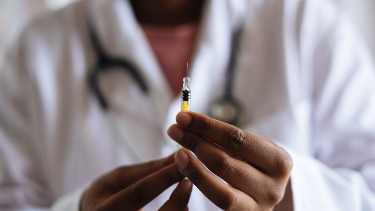 A doctor holds a needle filled with "gender-affirming" drugs.