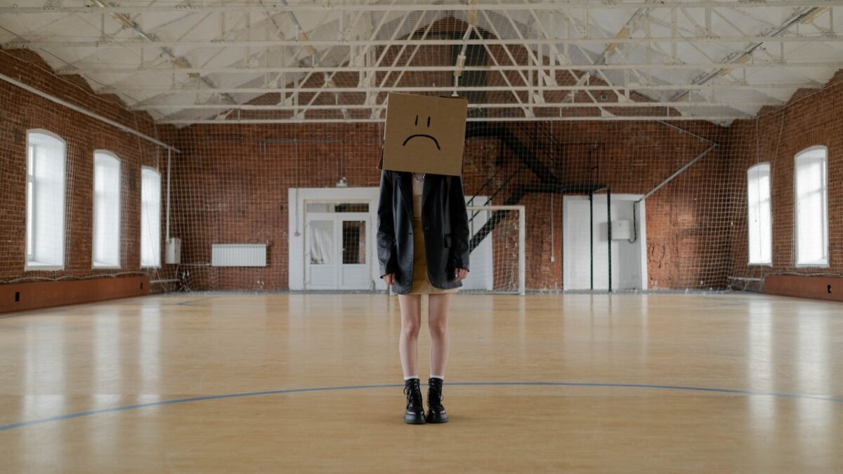 A child stands in a gym with a box over their head.