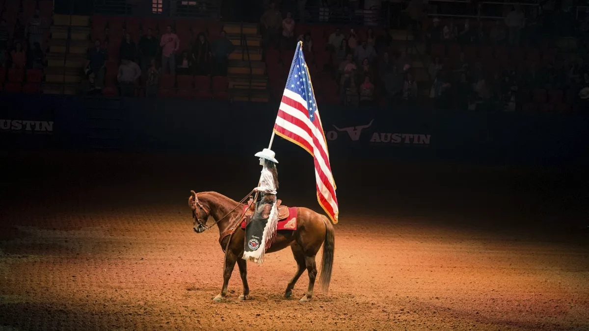 cowgirl holding usa flag on horse in arena