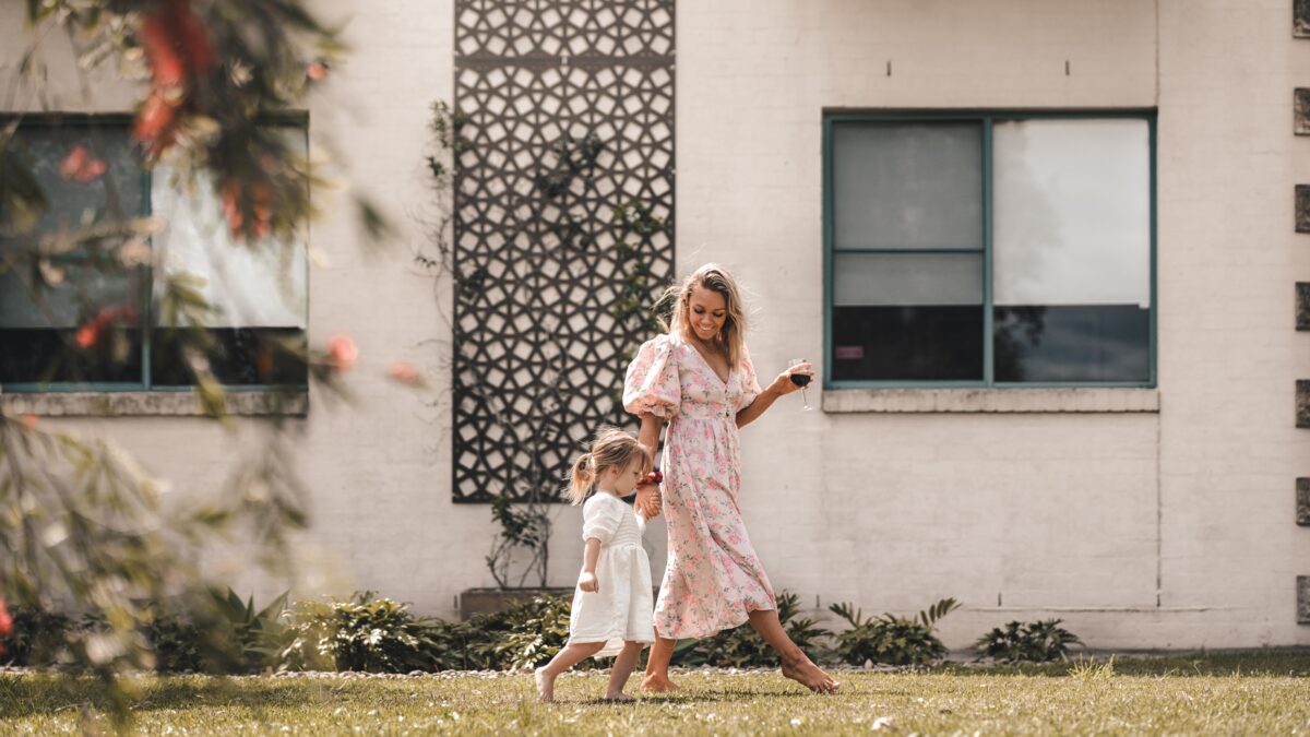 Mother and daughter walking in a yard wearing dresses.