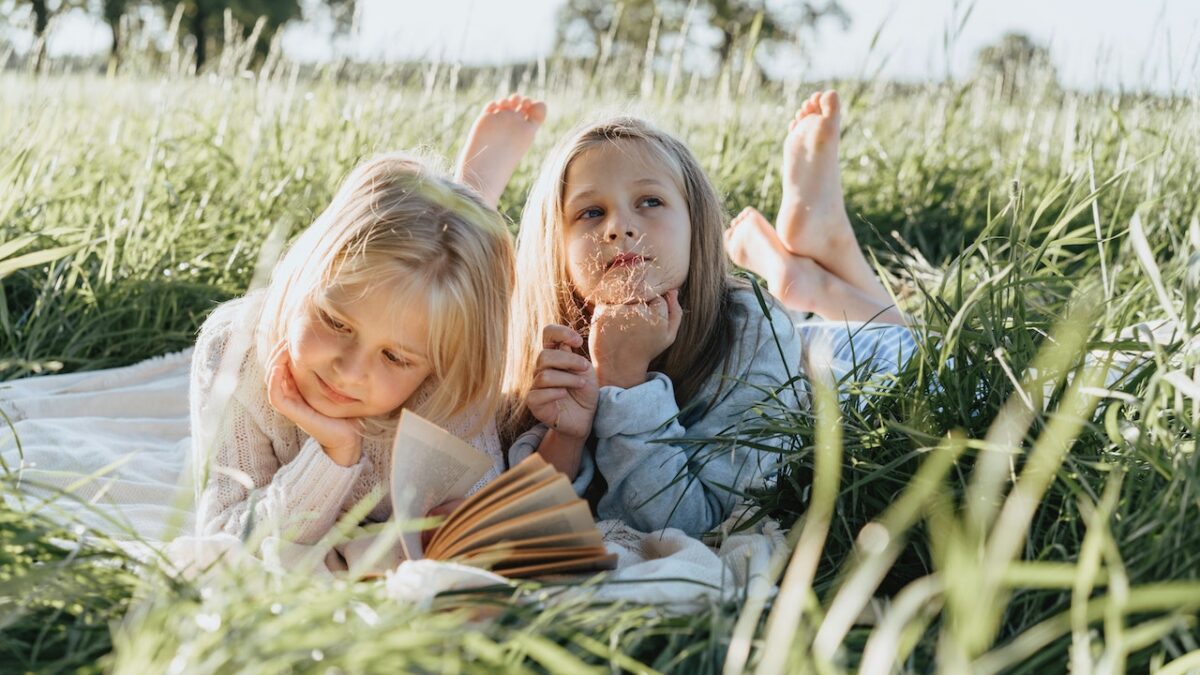 little girls lying in grass with books