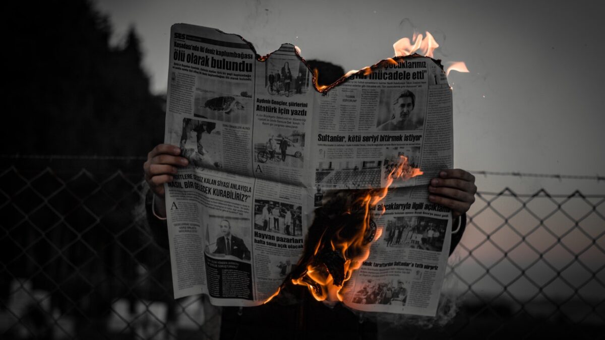 A person reads a burning newspaper outside.