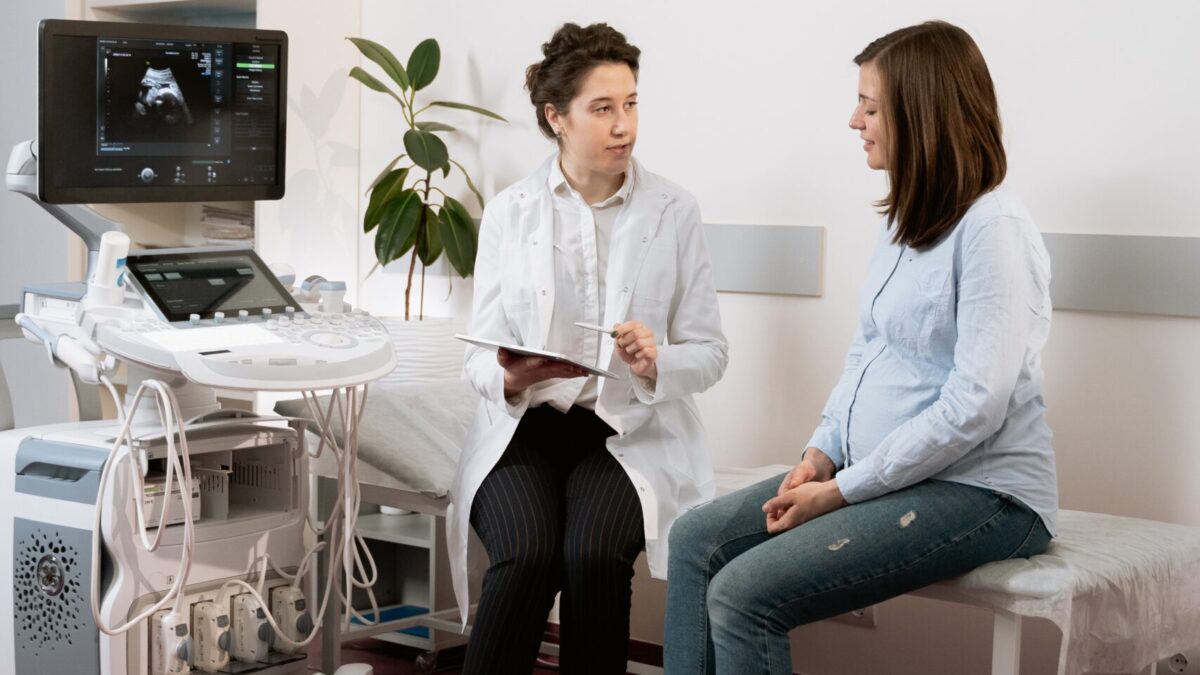 Pregnant woman sits with doctor next to ultrasound machine.