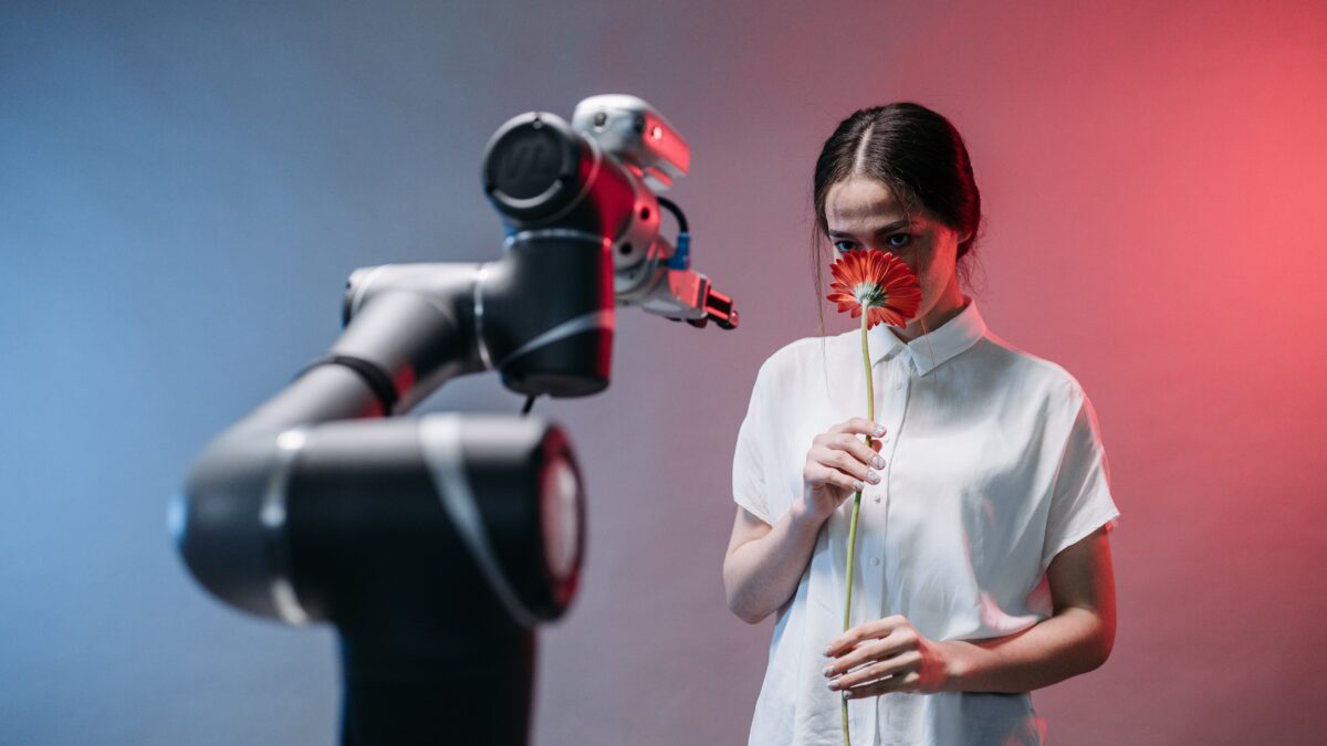 Girl sniffs red flower while standing next to a robotic arm