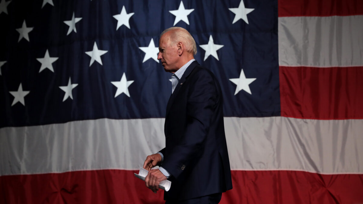 Joe Biden in front of the American flag holding a piece of paper
