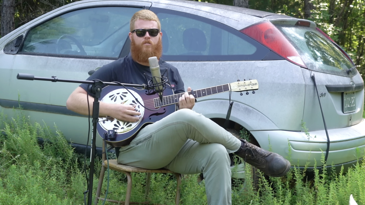 Oliver Anthony playing banjo guitar instrument outside by car