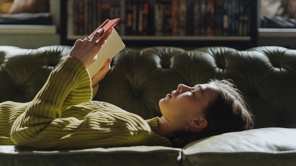 teen girl reading book laying on couch