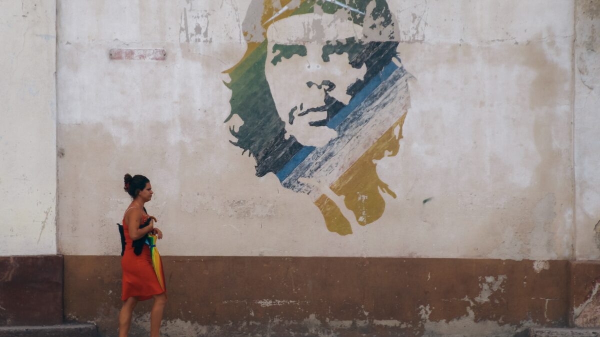 Woman in red dress walking under mural of Che Guevara.