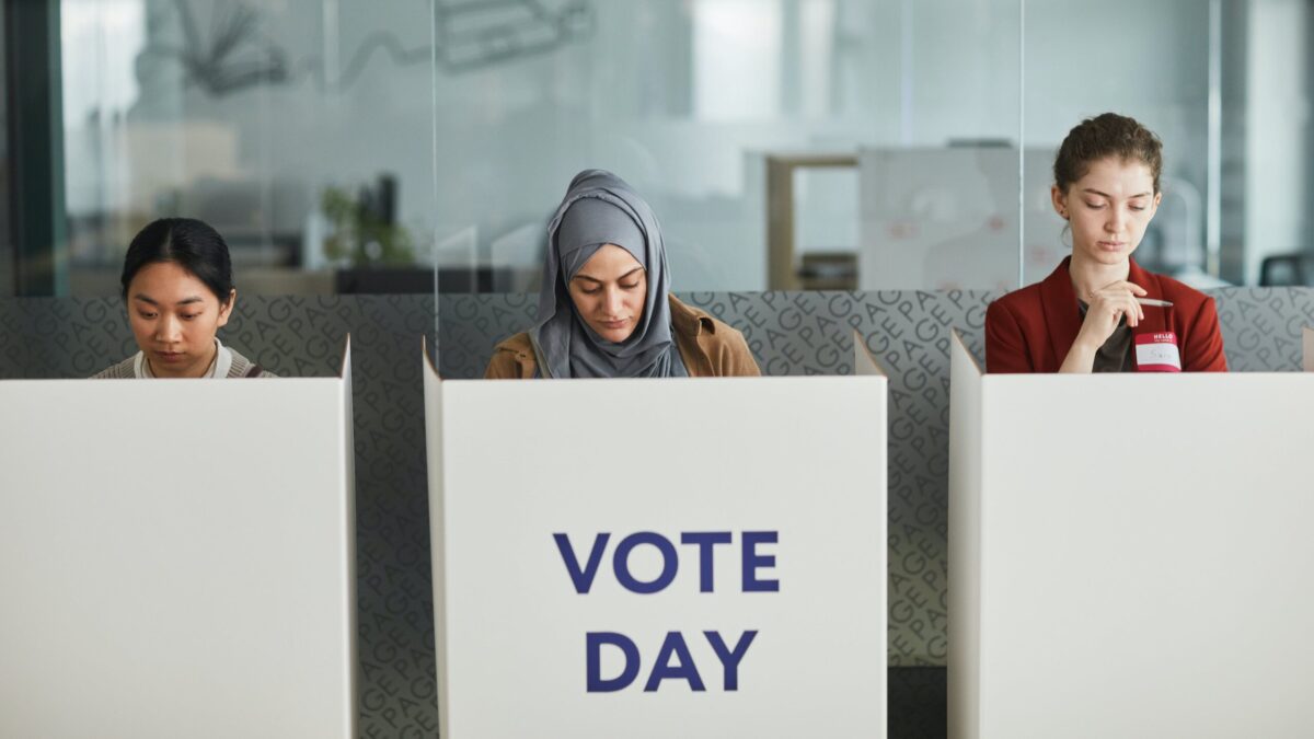 Three women stand behind voting booths, and the center booth reads "Vote Day."