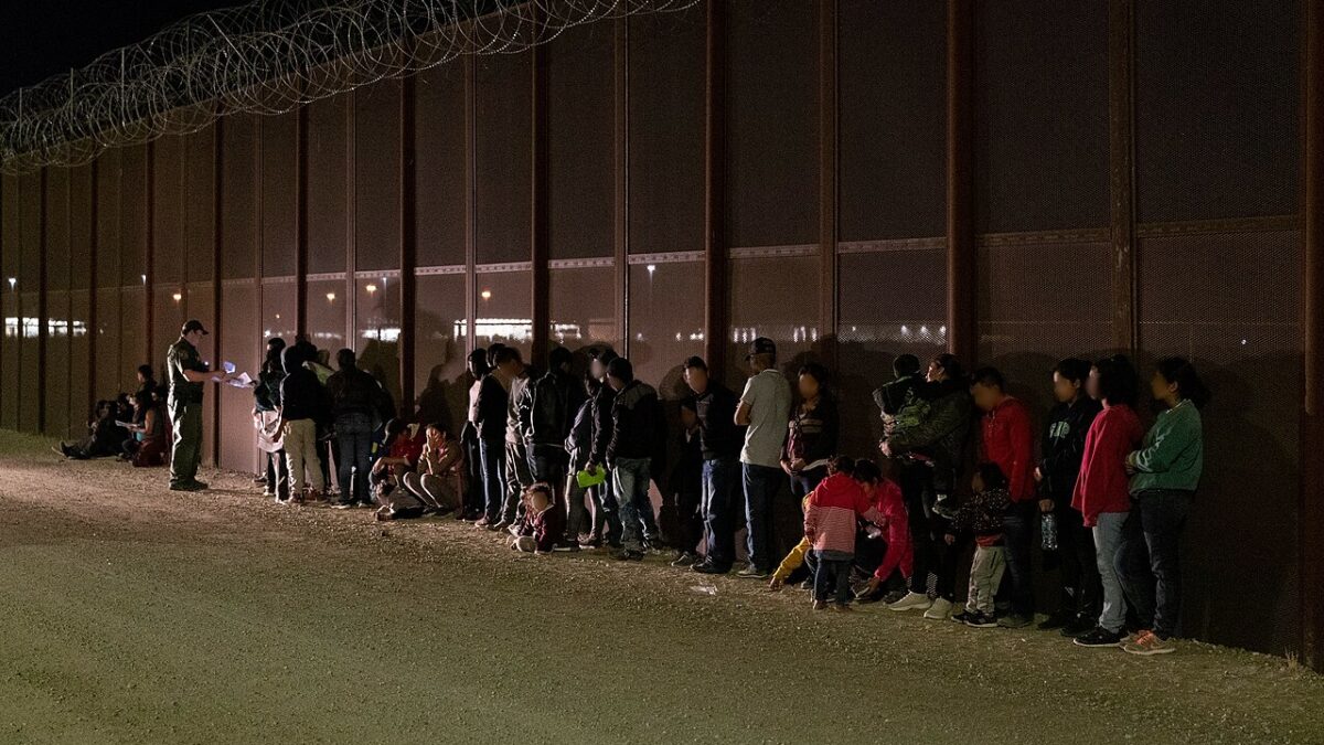 migrants wait along fence at the border