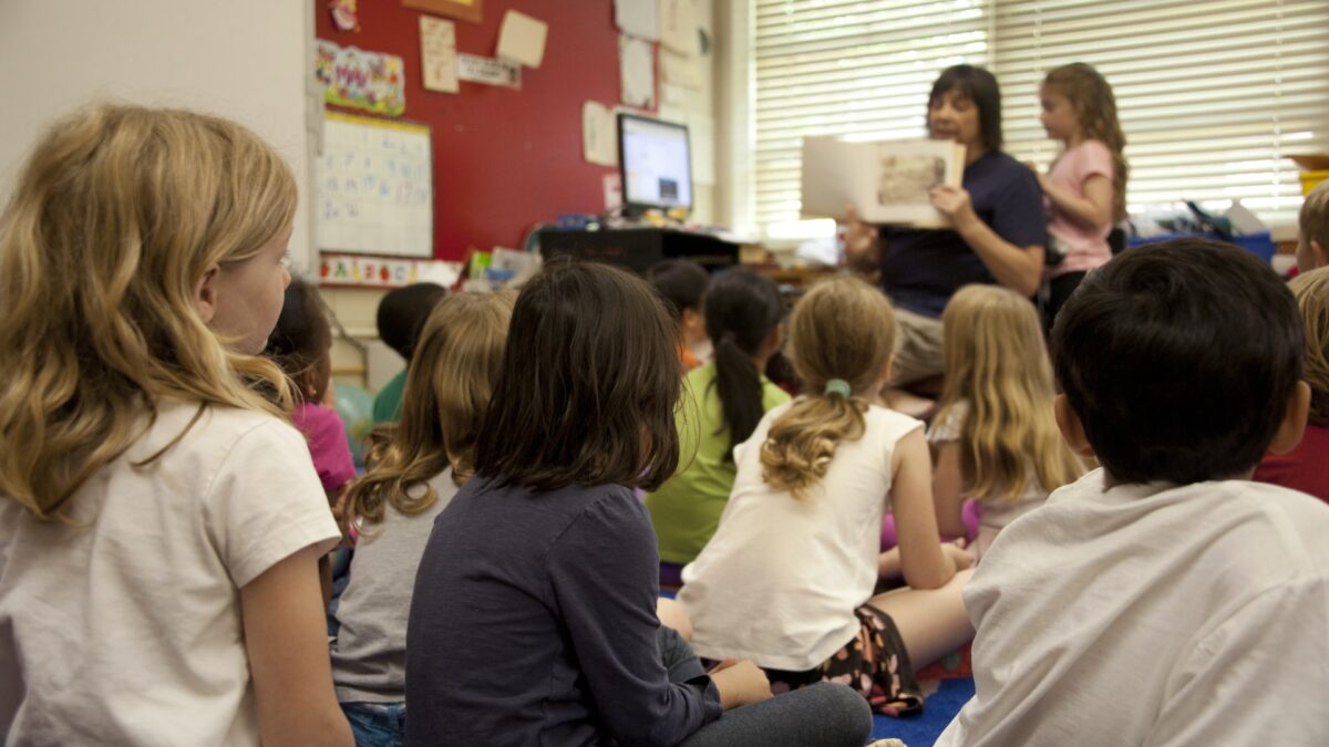kids sitting a room while a teacher reads them a book