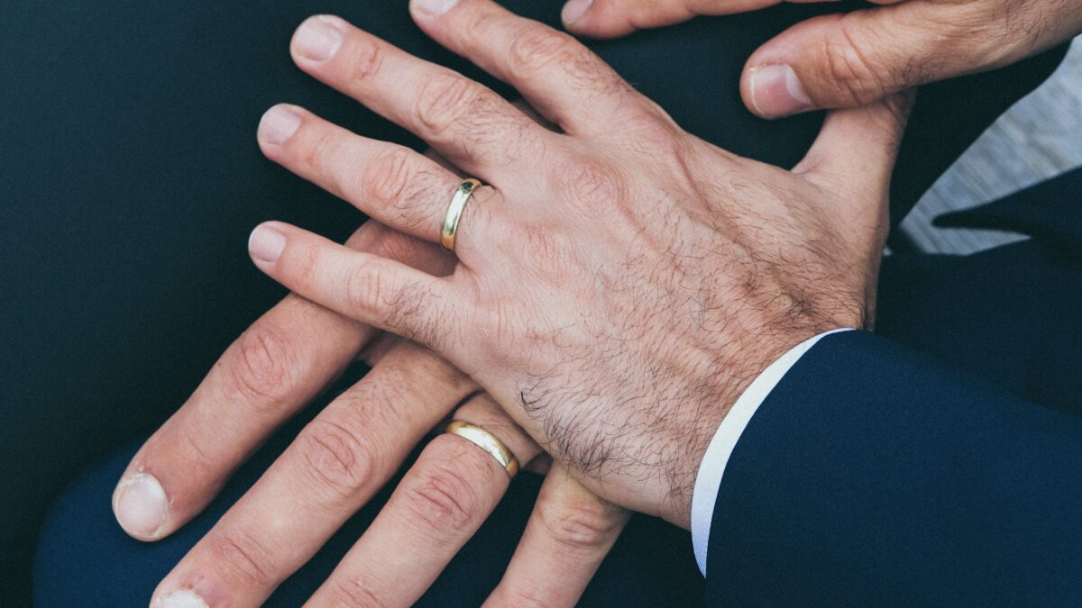 two men's hands with wedding bands stacked on top of each other