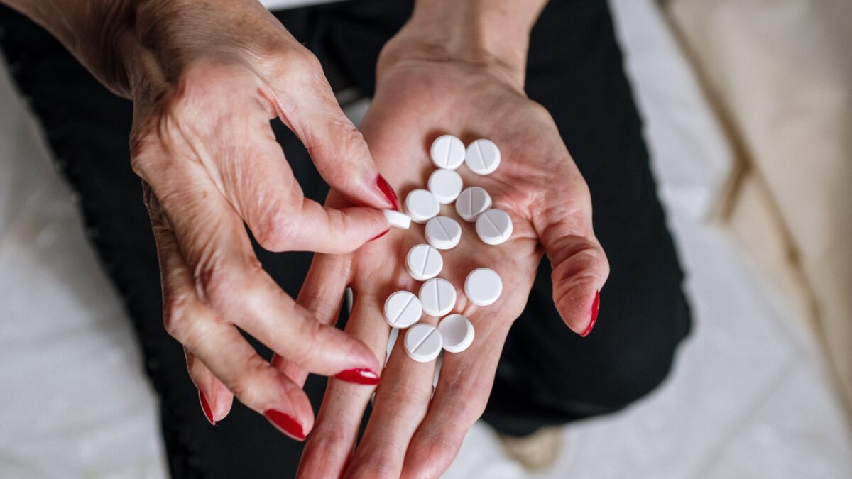 Woman holds many white pills in the palm of her hand.