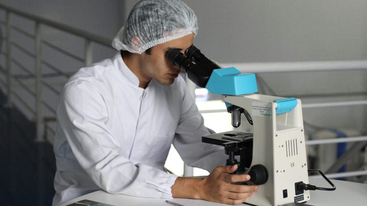 Man in a lab coat looking through microscope.
